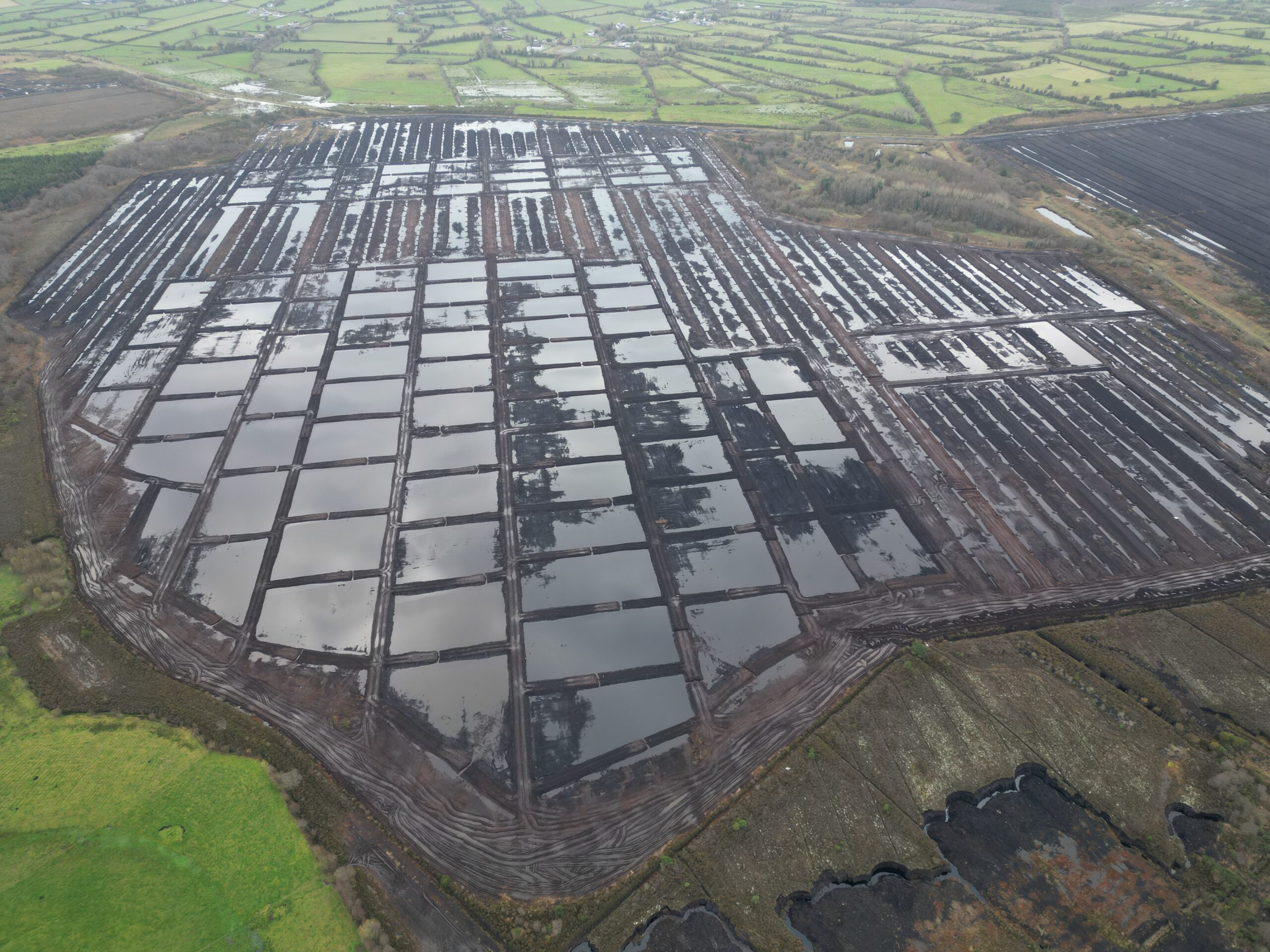 Aerial view of Ballaghurt Bog after restoration, featuring a mosaic of water-filled plots and rewet areas. Vegetation is beginning to return, and the layout reflects efforts to restore natural hydrology and habitat.